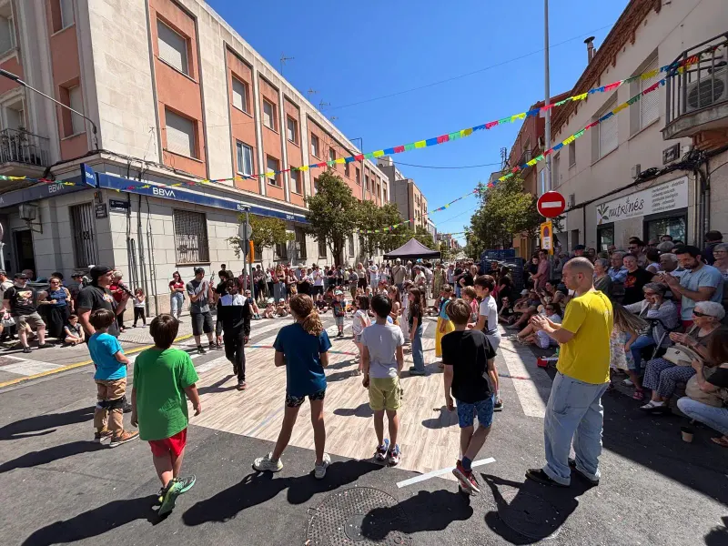Taller de breaking amb nens i nenes al mig del carrer durant la festa major de Sant Pere, amb veïns asseguts mirant
