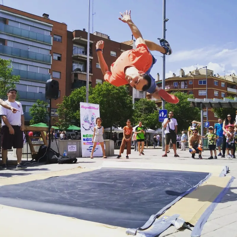 Un ballarí fent un salt mortal en una exhibició de breaking a l'aire lliure, amb veïns mirant al voltant de la pista
