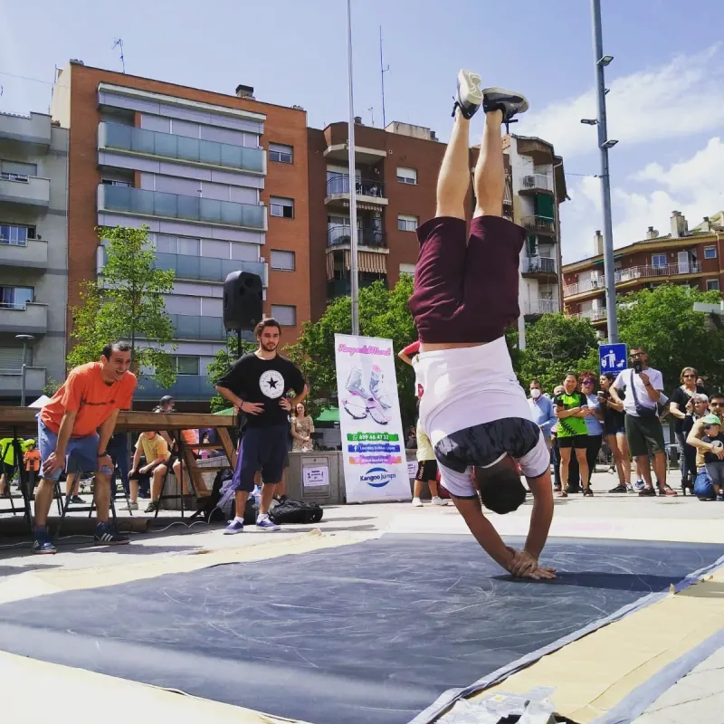 Un ballarí fent el pi sobre les mans a la pista, en una plaça plena de gent