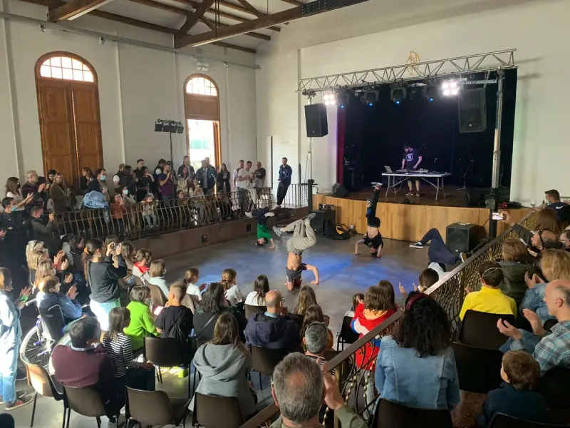 Exhibició de breaking en una sala plena de famílies assegudes al voltant de la pista